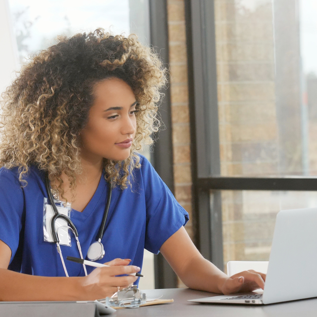 nurse wearing scrubs working on her laptop