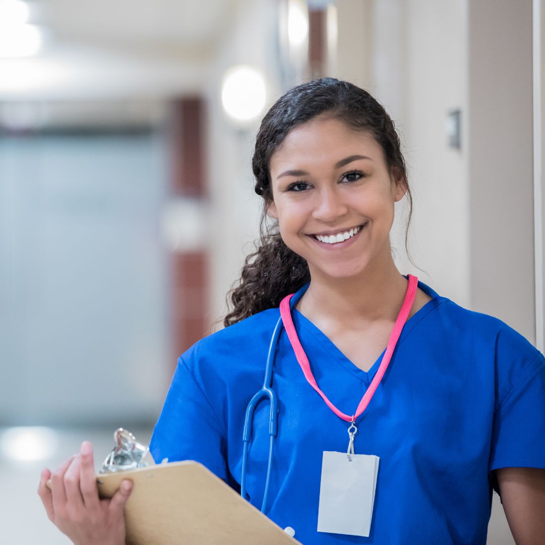 female nurse in blue scrubs smiling at the camera